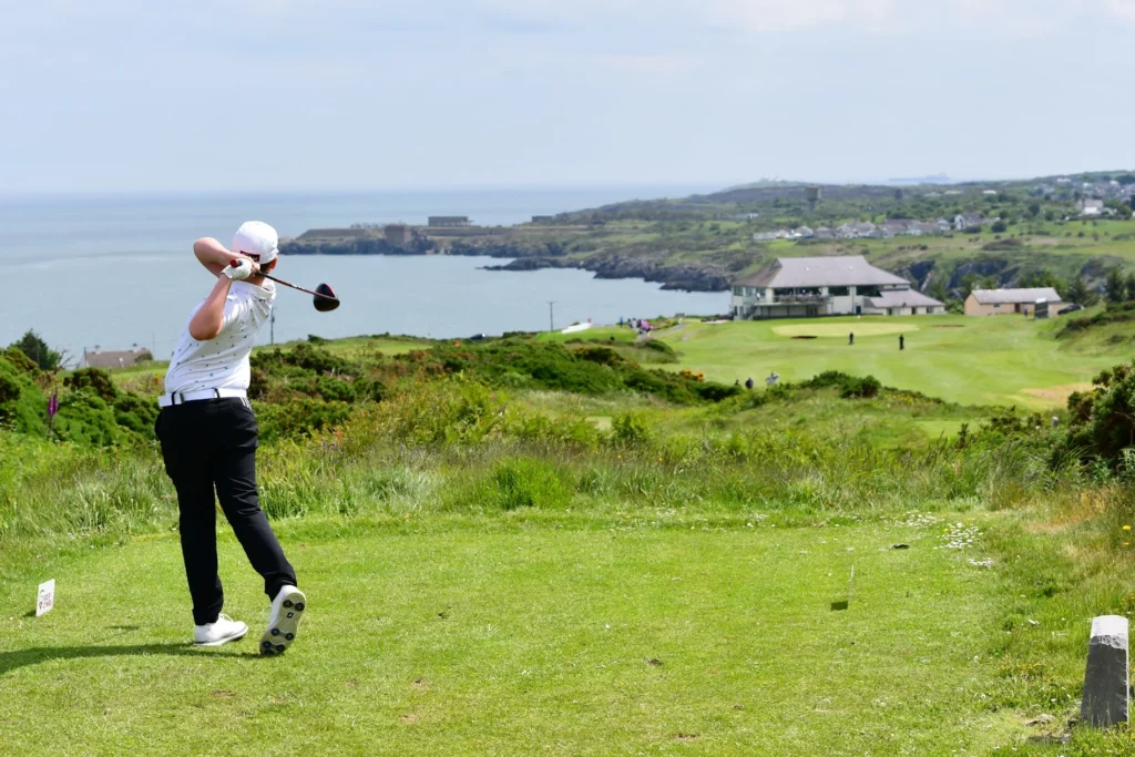A golfer with a white top finishes his follow through after driving on the 18th.