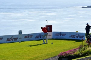 First tee, blue sea in the background, surrounded by Wales Golf signage with a competitor playing his first shot.